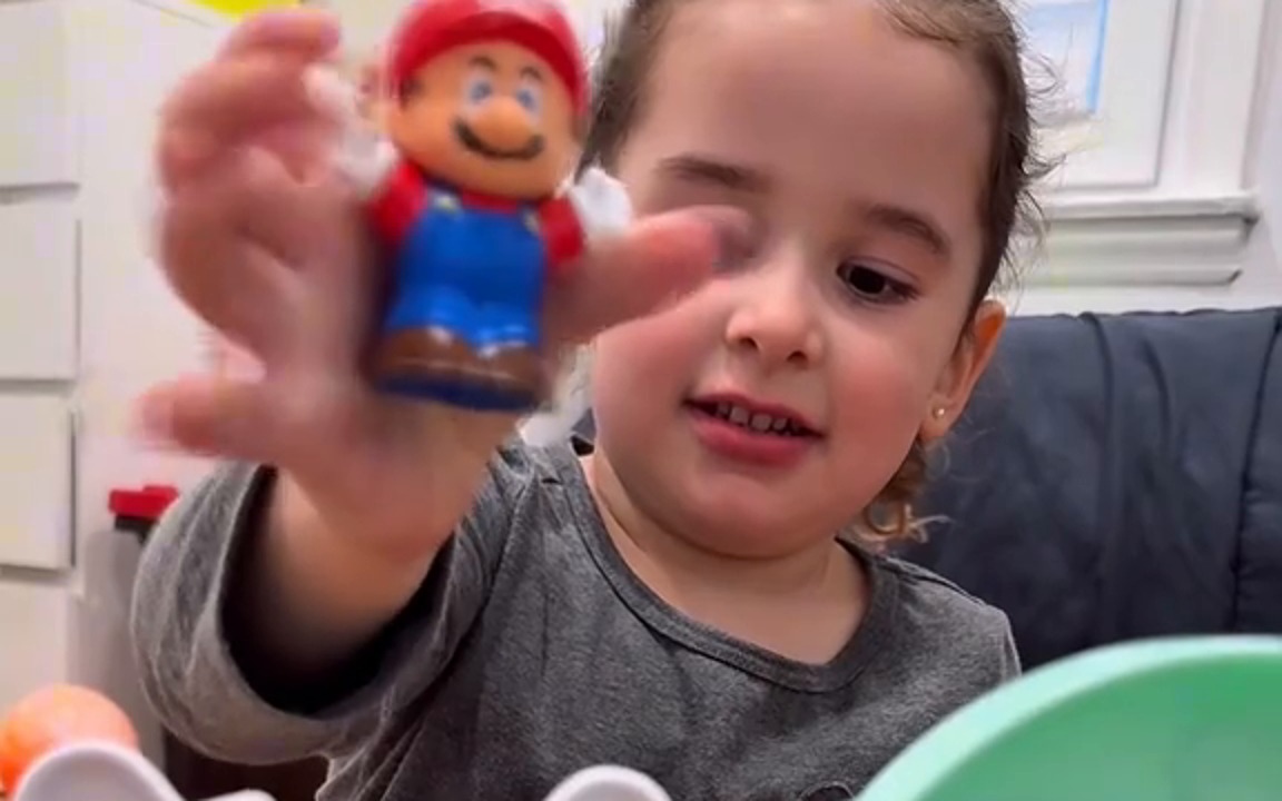 A young girl holding Little People Mario, Luigi and Toad figures from the Nintendo partnership launch content